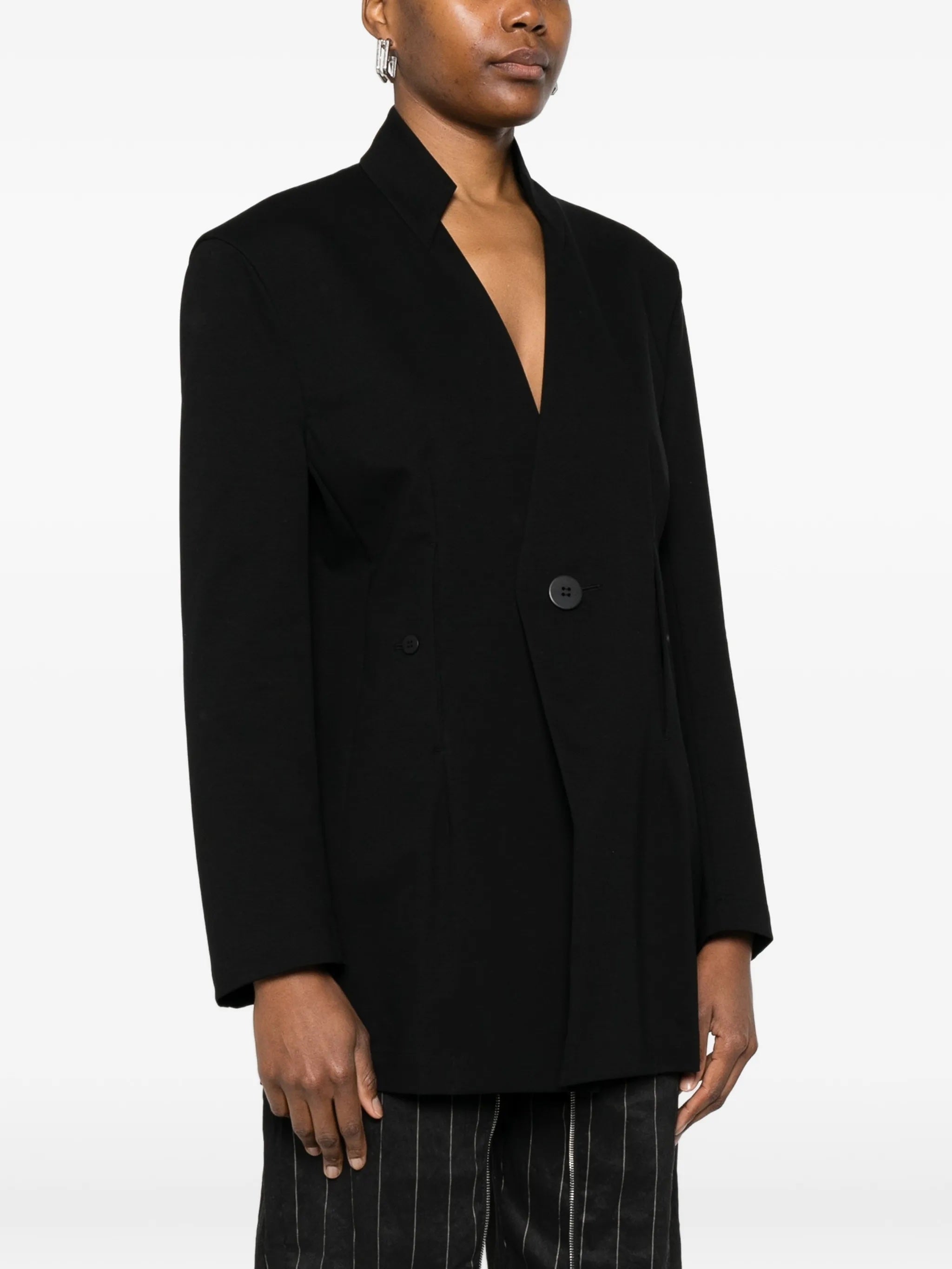 Close-up of model wearing the black, single-breasted blazer from Issey Miyake on a white background