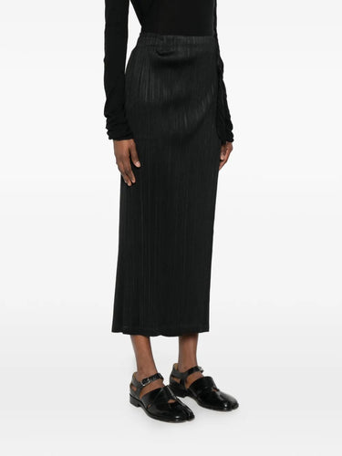 Model wearing the February SS26 Facade Pants in Black black pleated straight-leg pants with mid-rise waist and wrap detail, side view – Issey Miyake Pleats Please