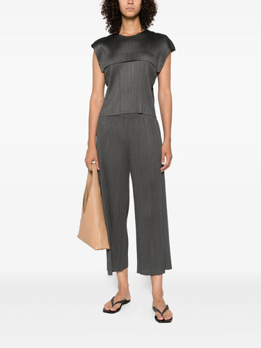 Woman wearing a black top and gray pants holding a beige bag on a white background