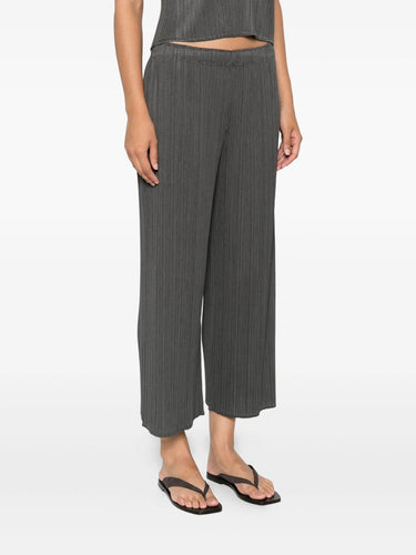 Woman wearing gray pleated pants from Pleats Please Issey Miyake on a white background