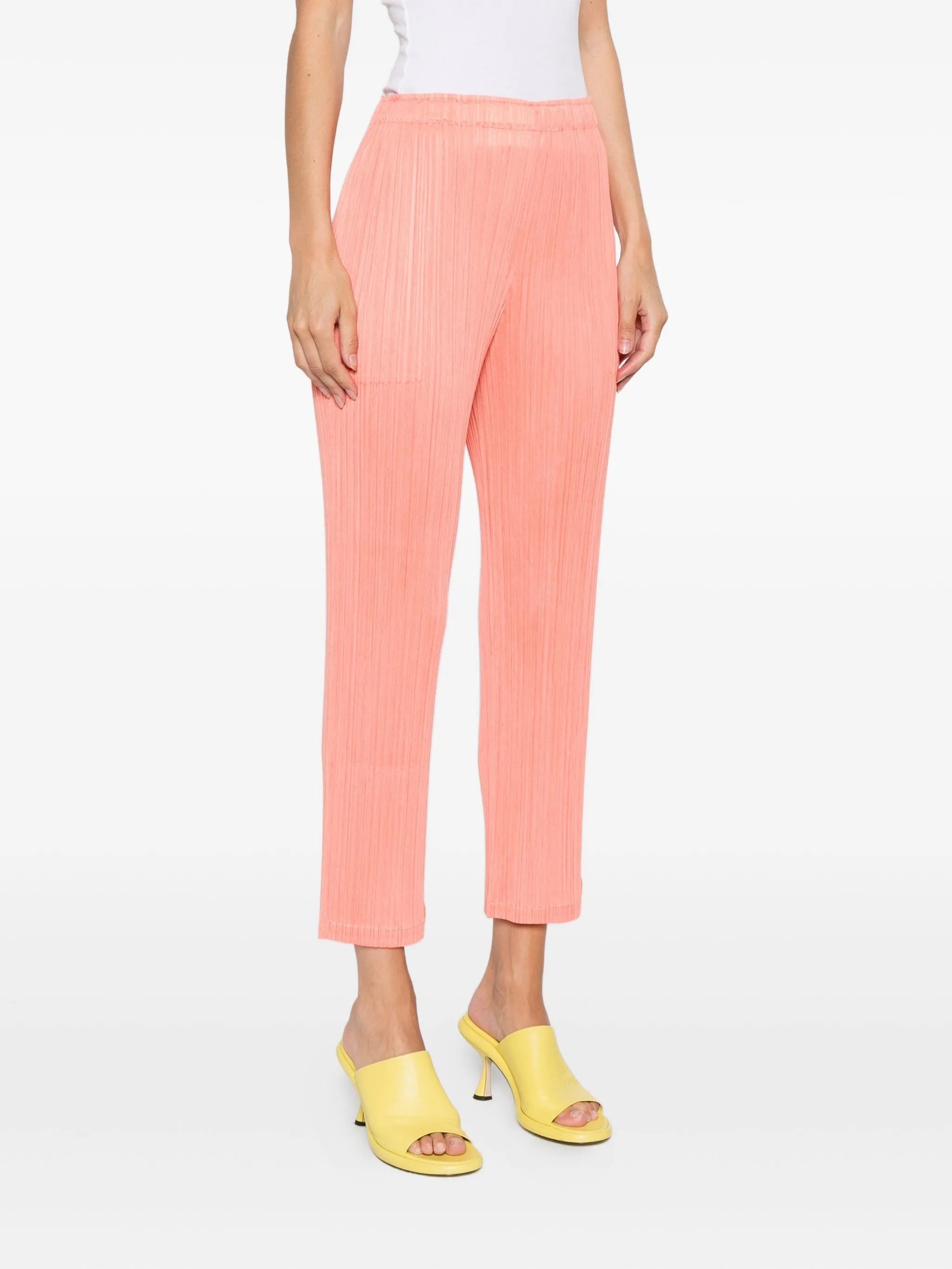 Person wearing coral pants with a white top and yellow sandals on a white background