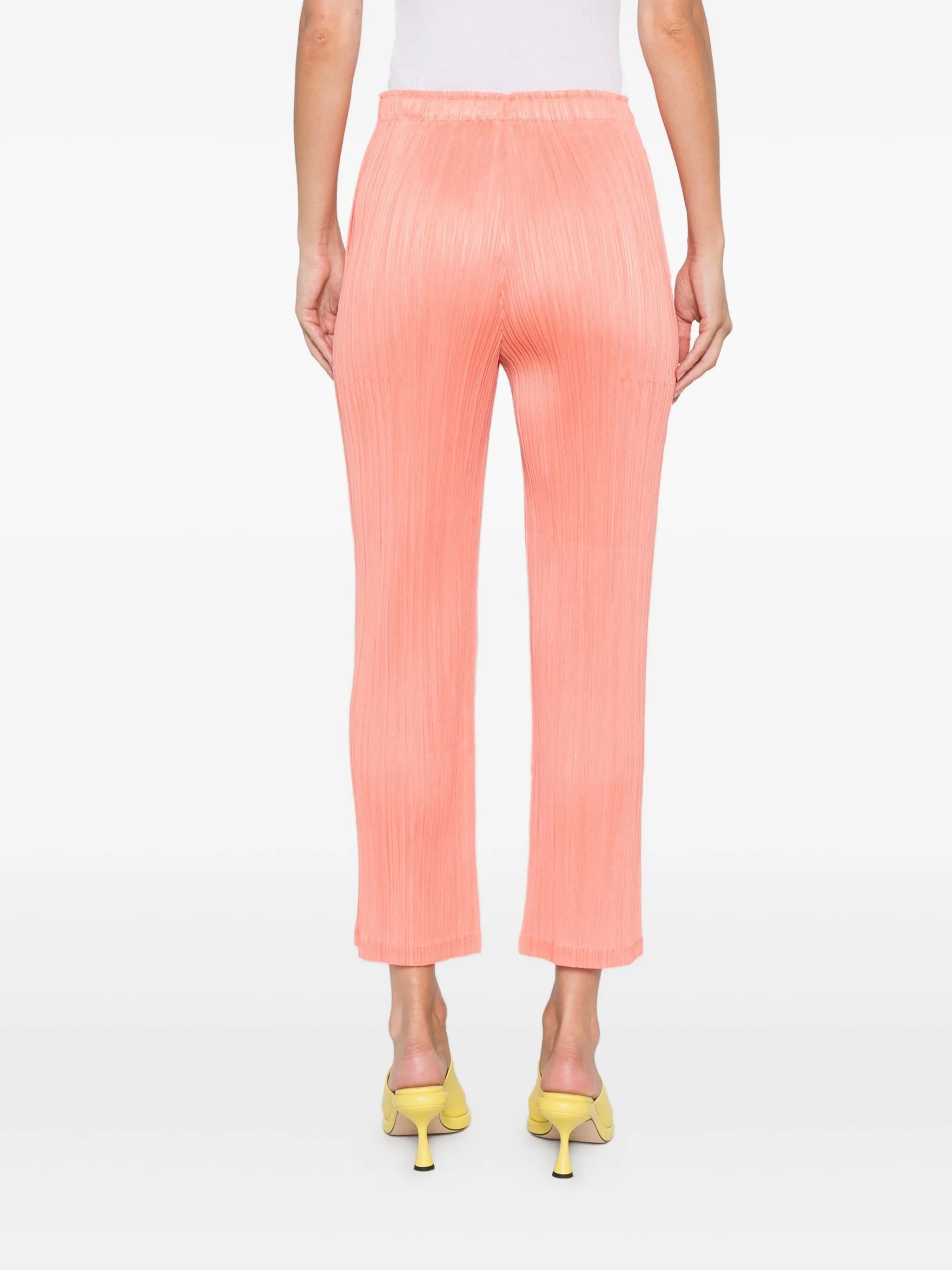 Person wearing coral pants with a white top on a white background
