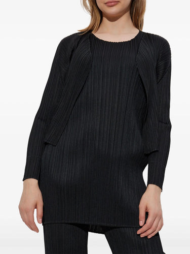 Woman wearing a black pleated outfit from Pleats Please Issey Miyake on a white background