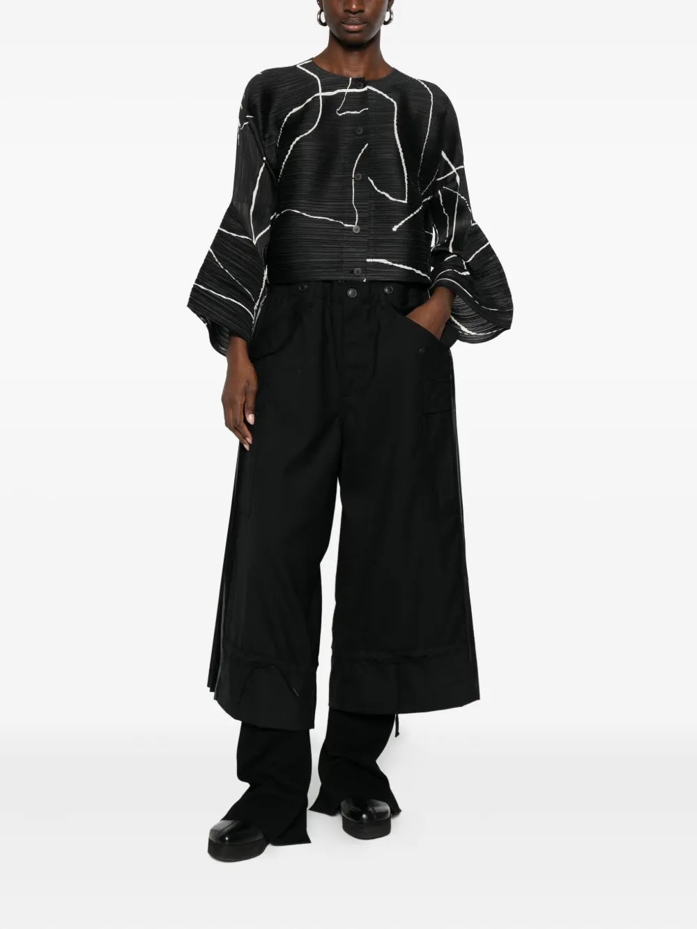 Person wearing a black and white patterned top with wide-leg pants on a white background