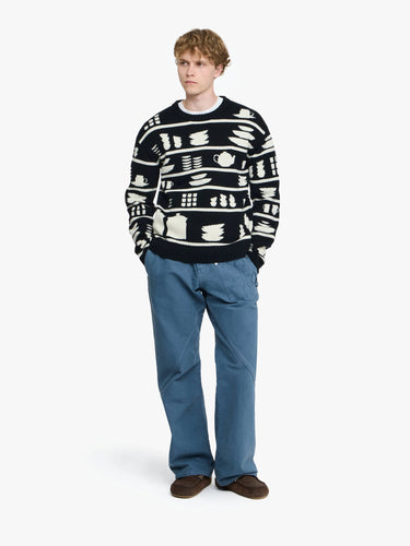 Person wearing a black and white patterned sweater with blue pants on a white background