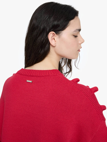 Woman wearing a red sweater with a visible brand logo on a white background
