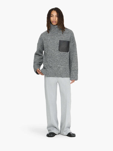 Person wearing a gray sweater with a black pocket and light gray pants on a white background