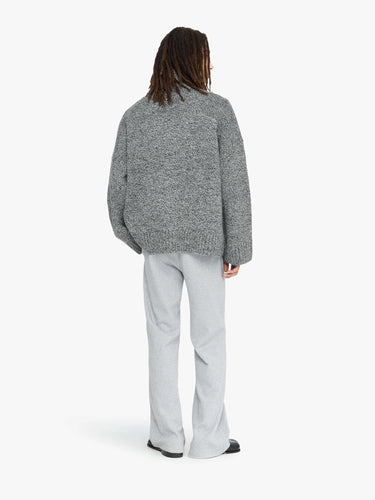 Person wearing a gray textured sweater and light gray pants on a white background