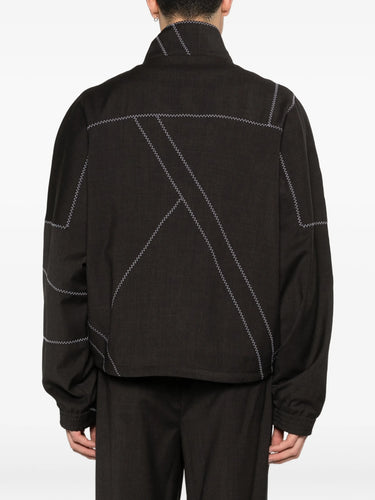 Back view of model wearing the dark brown jacket with white geometric contrast stitching from Kiko Kostadinov on a white background
