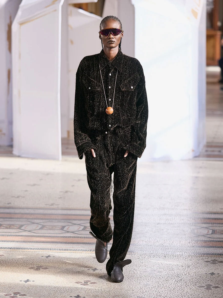 Kiko Kostadinov Weka Shirt in Hickory worn on the runway, showing the relaxed long-sleeve silhouette, textured dark fabric, button-front construction and utility-inspired chest detailing.