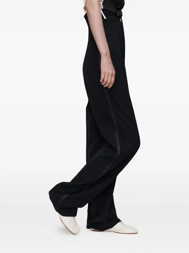Side view of a model wearing the black Maison Margiela women’s pants, highlighting the stripe detail along the leg and the high-waisted fit.