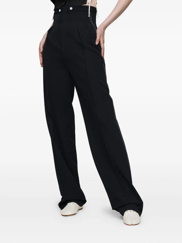 Front view of the model wearing the black Maison Margiela pants, showing the button fastening, high waist, and straight-leg cut.