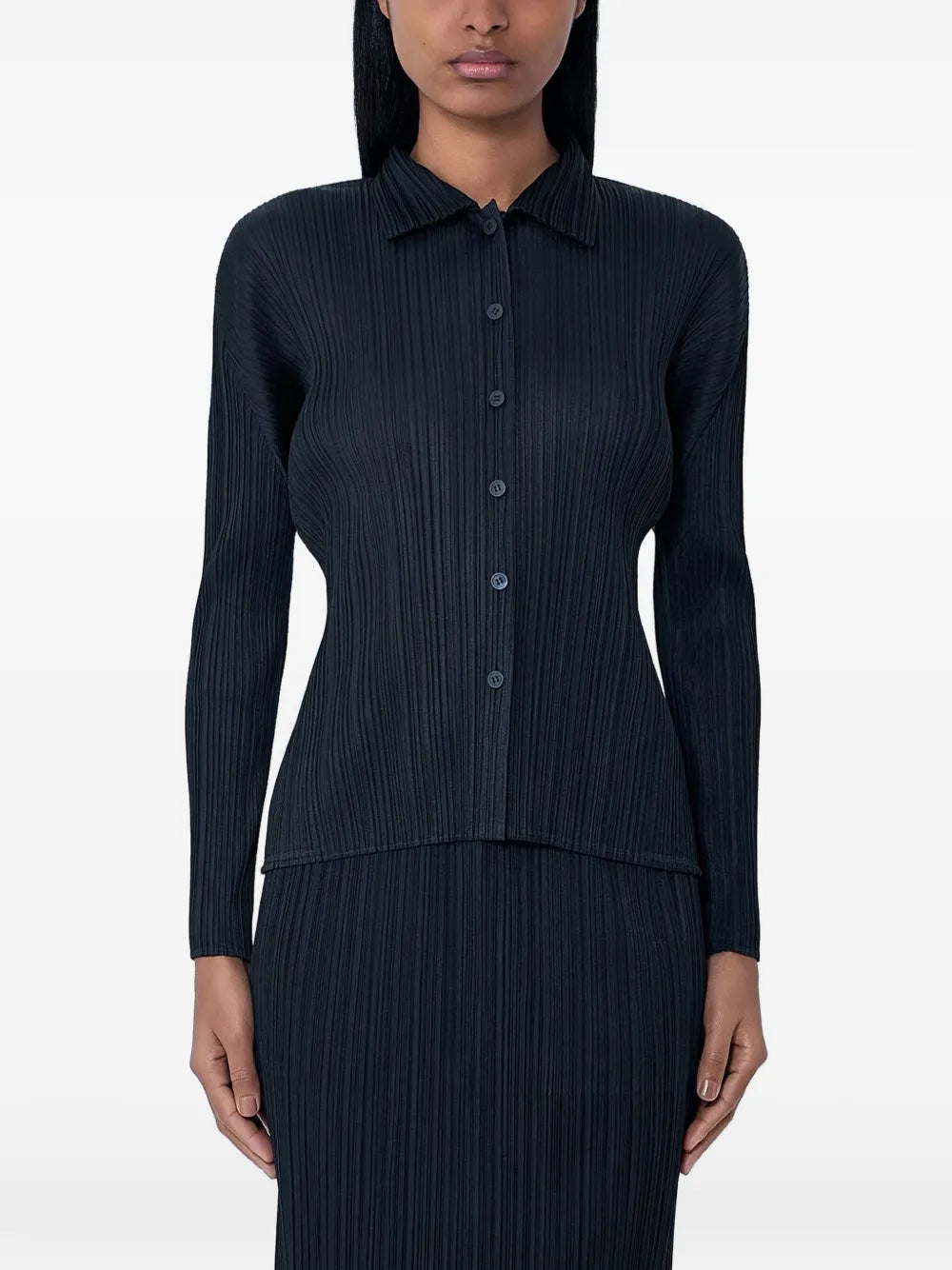 Modal wearing the black, pleated, button-up top with long sleeves from Pleats Please Issey Miyake on a white background
