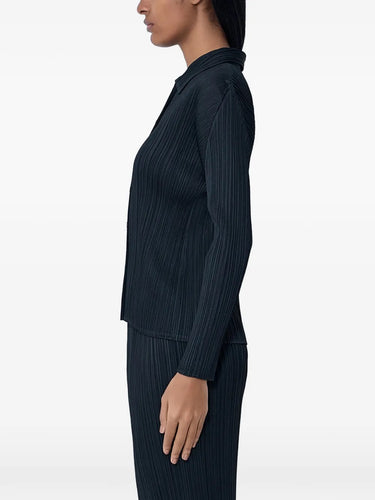 Side view of model wearing the black, pleated, button-up top with long sleeves from Pleats Please Issey Miyake on a white background