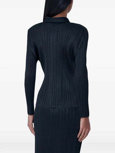 Back view of the model wearing the black, pleated, button-up top with long sleeves from Pleats Please Issey Miyake on a white background