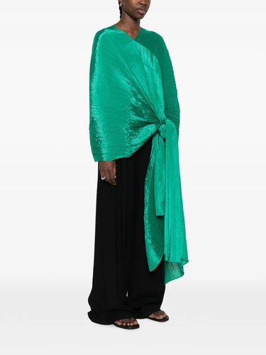 Side view of a model wearing the green pleated top called Madam T by Pleats Please Issey Miyake on a white background