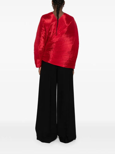 Back view of a model wearing the red pleated top called Madam T by Pleats Please Issey Miyake on a white background