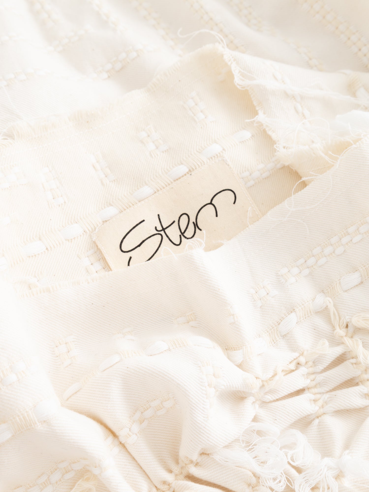 Stem Basket Tee in off-white, close-up of interior Stem label against woven basket-weave fabric