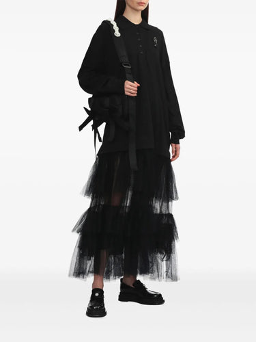 Person wearing a black outfit with a layered tulle skirt on a white background