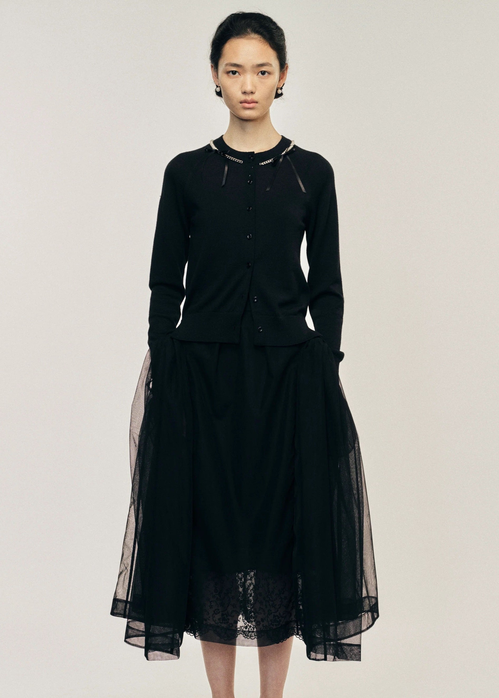 Woman wearing a black cardigan with a sheer overlay on a plain background