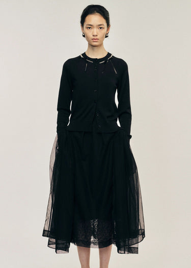 Woman wearing a black cardigan with a sheer overlay on a plain background