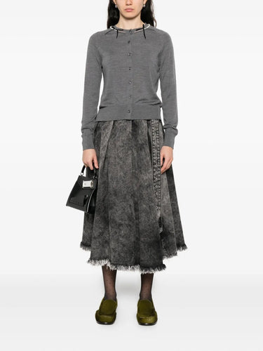 Person wearing a gray cardigan and dark denim skirt on a white background