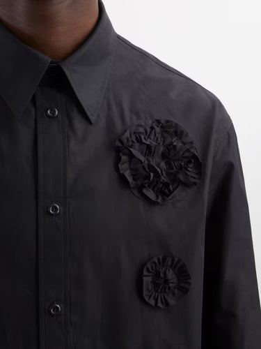 Close-up detail of a man wearing the black shirt with flower frill details from Simone Rocha on a grey background