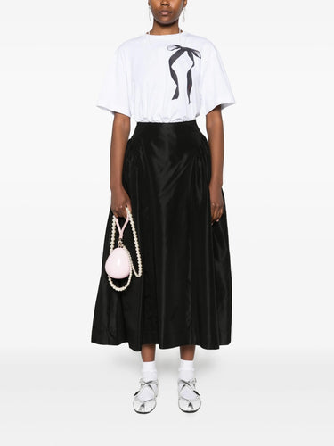 Person wearing a white t-shirt with a graphic design and a black satin skirt, holding a pink bag on a white background.