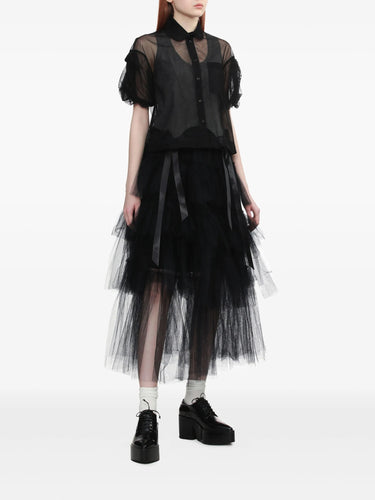 Person wearing a black outfit with sheer top and tulle skirt on a white background