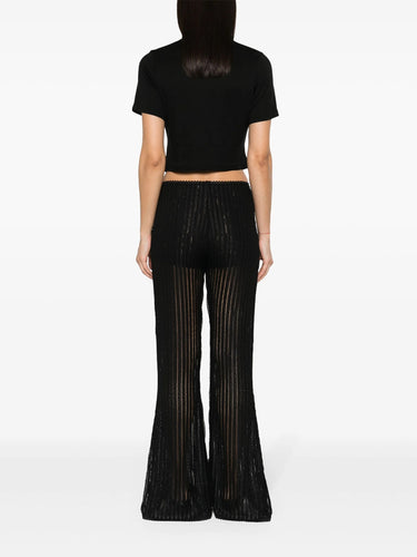 Person wearing a black crop top and black flared pants on a white background