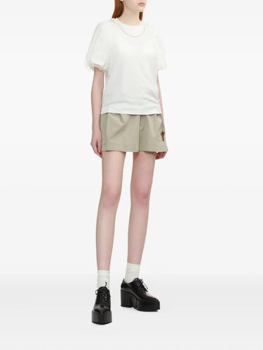 Person wearing a white top and beige shorts on a white background