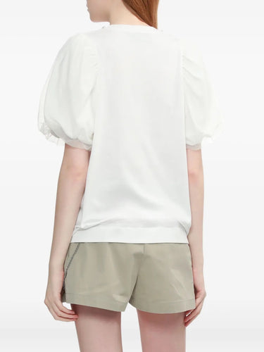 Person wearing a white top with puffy sleeves and beige shorts on a plain background