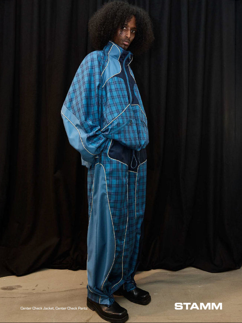 Stamm Exchange Center Check Jacket in Blue Check worn with matching trousers, featuring an oversized silhouette, high collar, contrast blue panels, curved seam detailing and light piping.