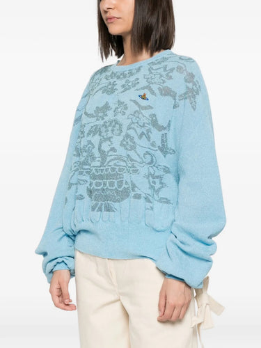 Model wearing Jules Jumper in Aqua by Vivienne Westwood, side view showing relaxed fit and voluminous long sleeves of aqua blue floral jacquard jumper with ribbed hem, Spring/Summer 2026