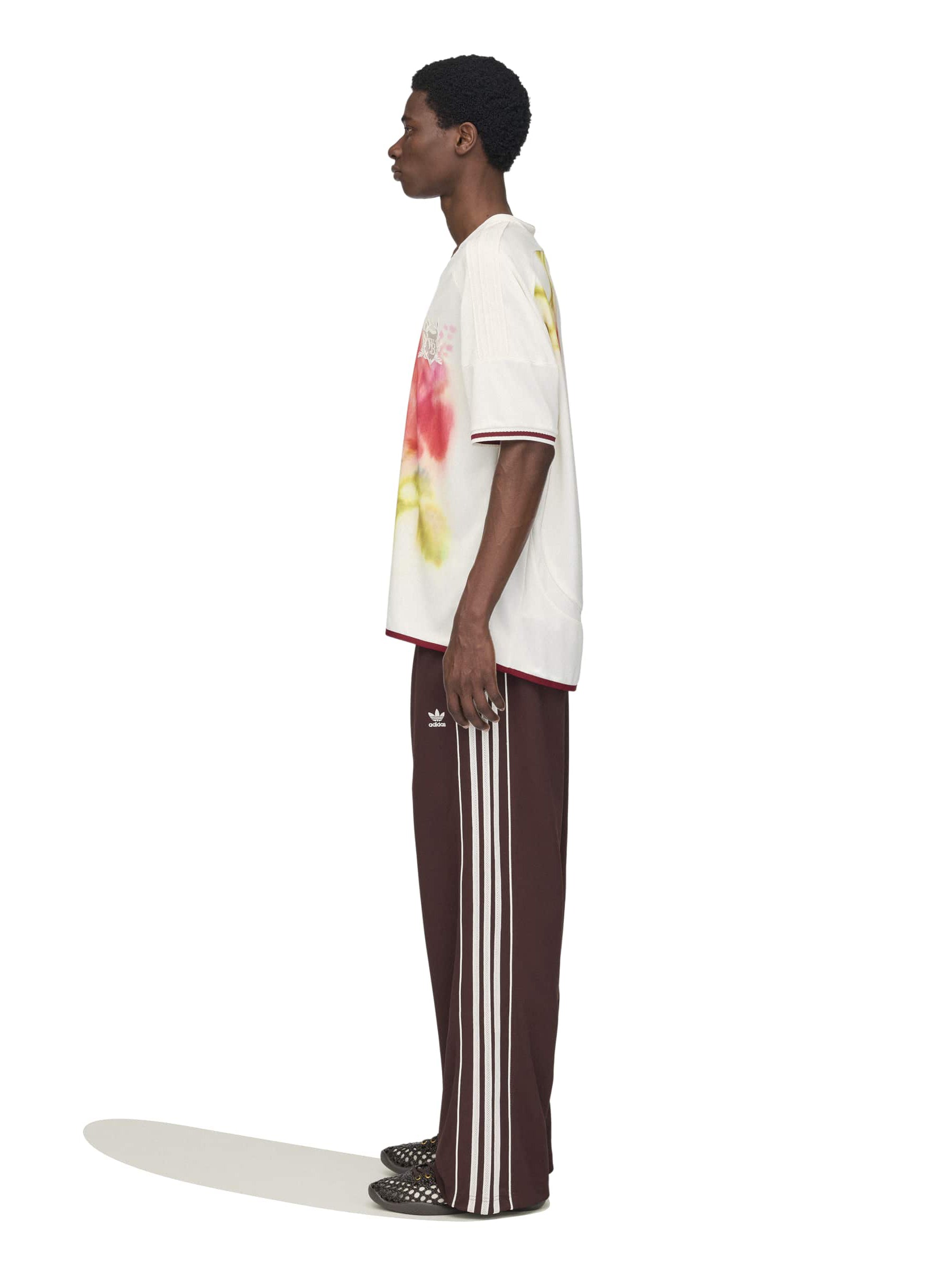 Model wearing the Wales Bonner x Adidas Track Pants in Shadow Brown shadow brown wide-leg track pants with white three-stripe detail, side view – Wales Bonner x Adidas SS26