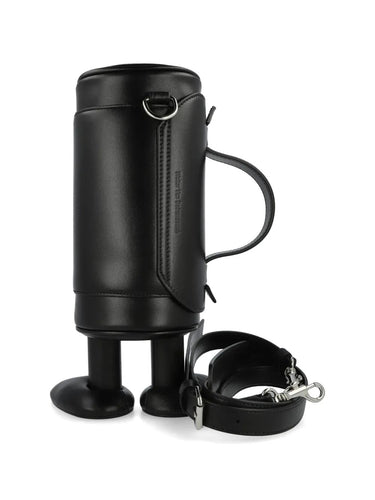 My Cilinder Friend Bag in Comb. I Black by Walter Van Beirendonck, side view of black leather cylindrical bag with sculptural footed base, detachable shoulder strap, white circle appliques and red logo charm