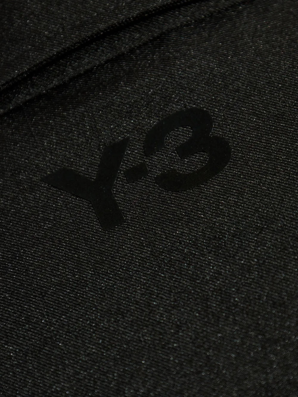 Close-up of a textured black fabric with a 'Y-3' logo on a dark background