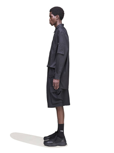 Side view of a male model wearing the Y-3 Sport Uniform Cargo Shorts in Black, emphasizing the wide silhouette and twill fabric structure.
