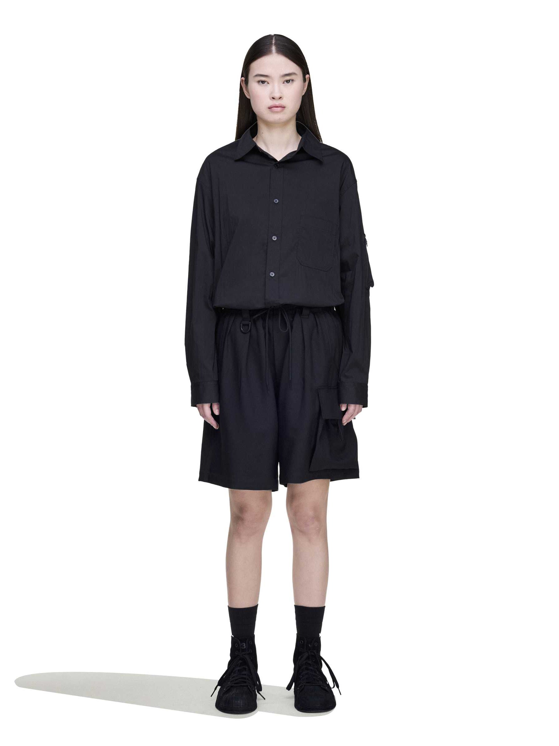 Front view of a female model wearing the Y-3 Sport Uniform Cargo Shorts in Black, showing the oversized silhouette and versatile streetwear look.