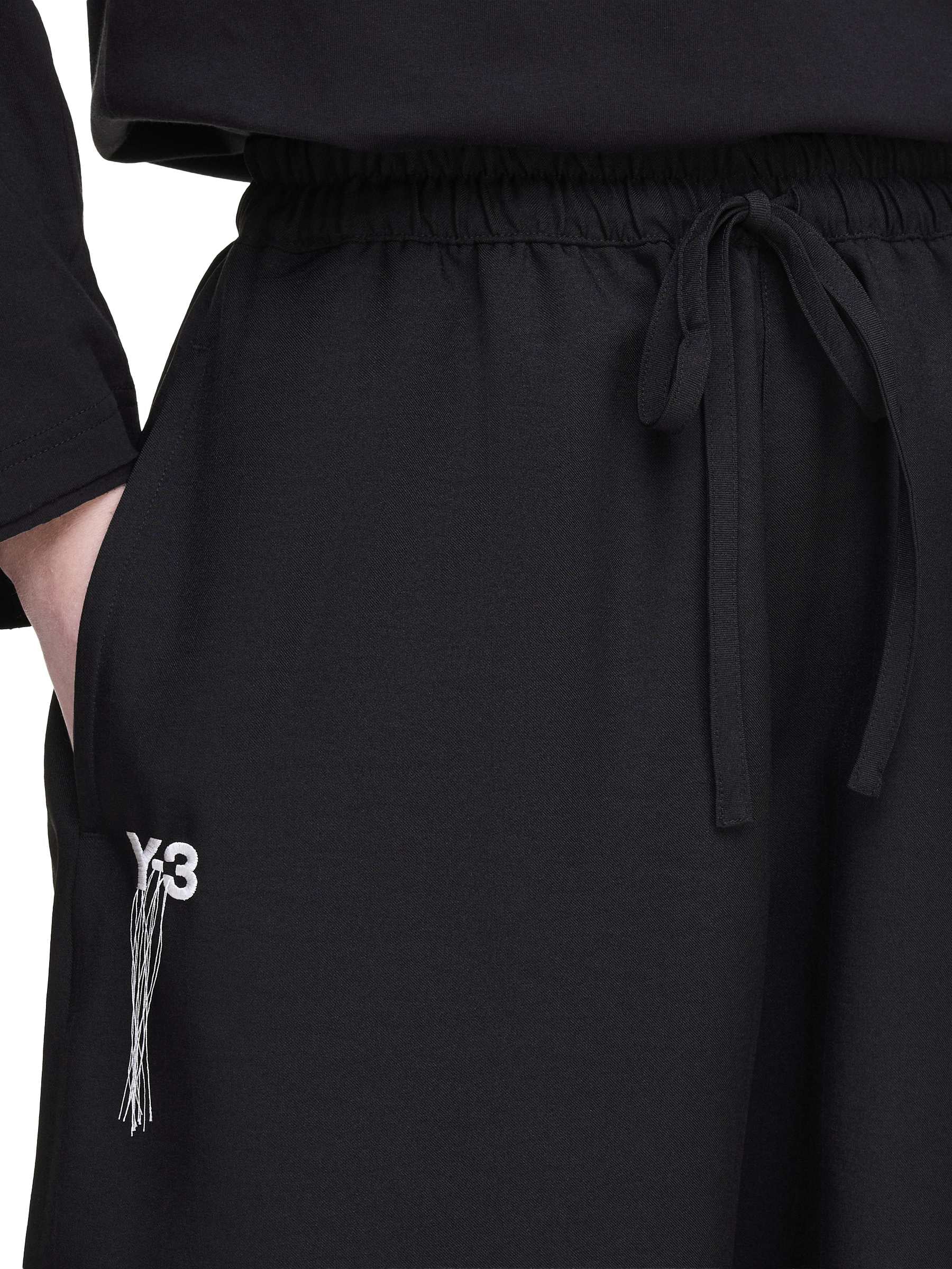 Front close-up of the Y-3 Summer Run 3-Stripes Shorts on a female model, highlighting the Y-3 logo embroidery with hanging threads.