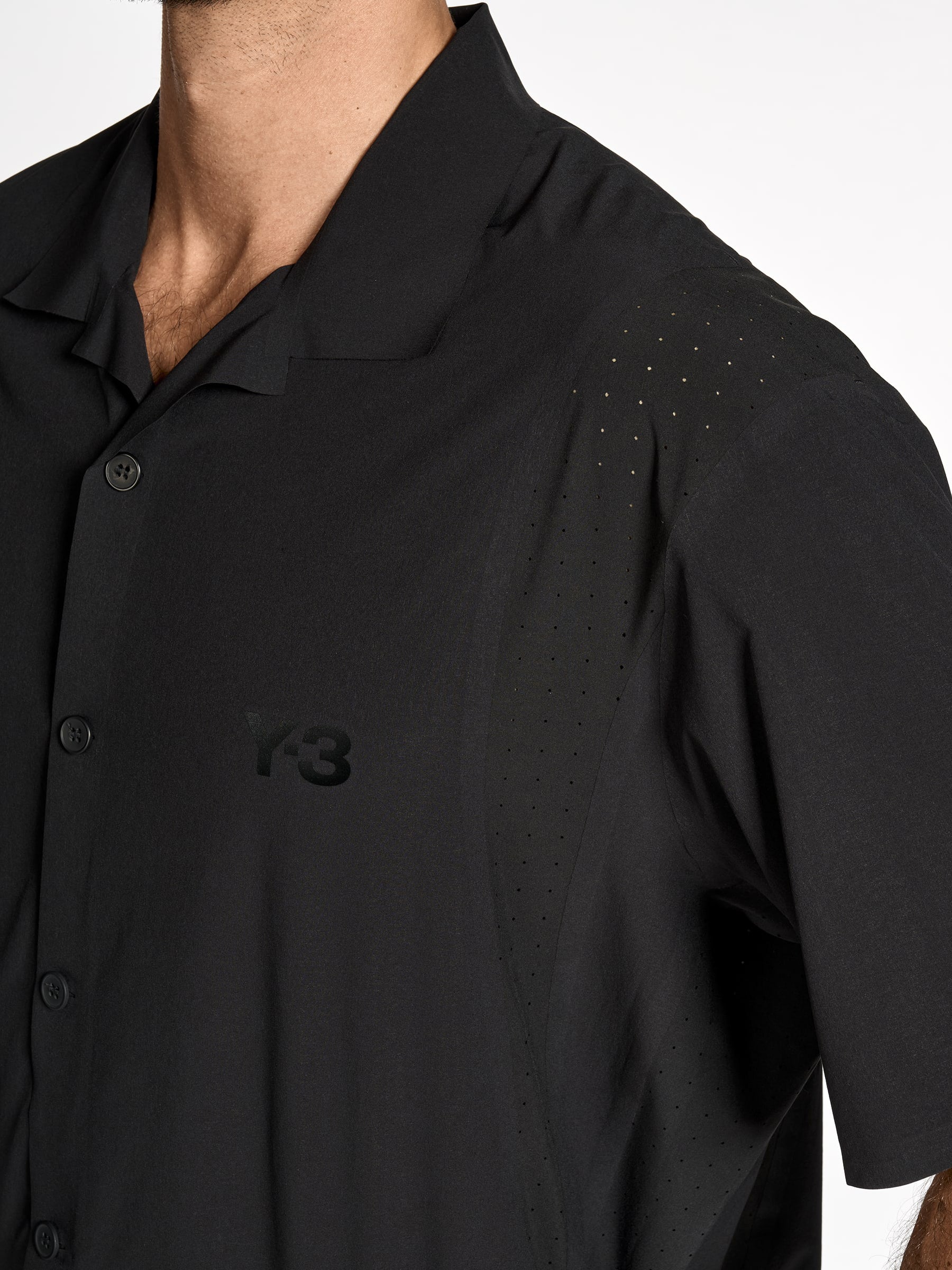 Top-front close-up of a model wearing the Y-3 Ultralight Woven Shirt in Black, highlighting the centre-front button closure, short sleeves, and subtle tonal Y-3 logo.