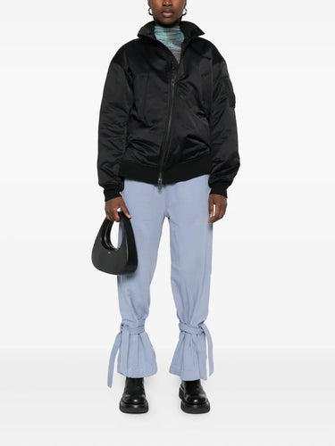 Person wearing a black jacket, light blue pants, and holding a black handbag on a white background