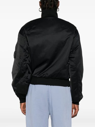 Person wearing a black bomber jacket and light blue pants on a white background